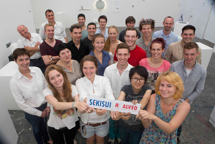 Juroren und Design-Studenten stehen zusammen. In der vorderen Reihe halten vier Personen Schild in die Kamera auf dem das Firmenloge der Sekisui Alveo AG zu sehen ist.