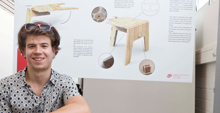 Eine Person, die sich die bunte Sonnenbrille in die Haare geschoben hat, steht vor einer Designzeichnung.