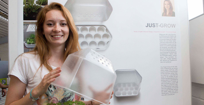 Eine Person hält einen transparenten Behälter in beiden Händen, der zu einem mini Gewächshaus gehört.