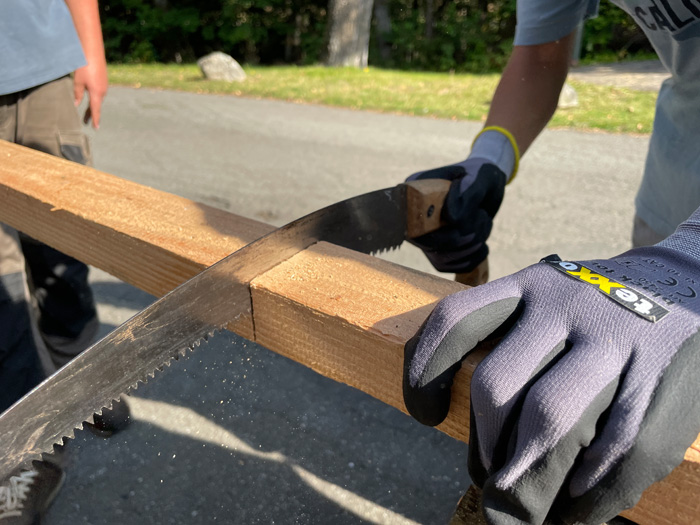 Eine Person mit Socherheitshandschuen sägt einen Balken.